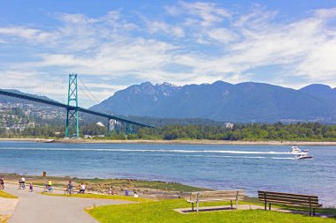Stanley Parkı içinde iz ile yerli halk ve turistler yaz, Vancouver Bc, Kanada güzel bir gün. Lions Gate Köprüsü, motorbot ve karlı zirveleri ile Dağlık ridge manzara.