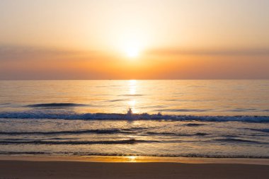 Güneş doğarken kumlu Akdeniz beach sıçramasına dalga ile. Sunrise yansımaları ve ufukta yelkenli ile denize.