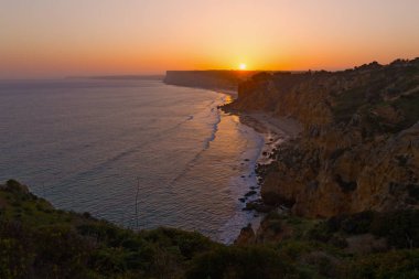 Güneş uzak bir uçurumun üzerinden Lagos, Portekiz günbatımında aşağı gider. Panoramik okyanus kıyı şeridi gün batımında.