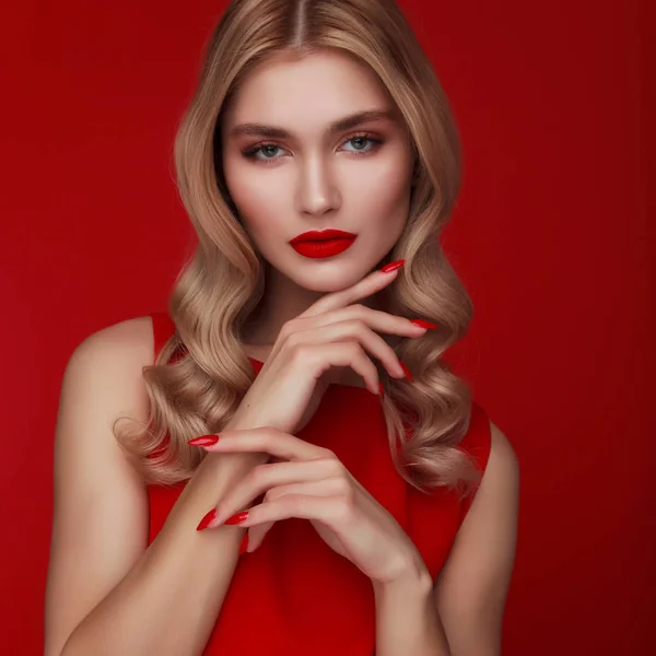 赤のドレスでファッショナブルなブロンドの女性のスタジオショット ハリウッドの髪型と赤い唇赤い釘だ魅力的なメイクアップと巻きファッションモデル 赤い背景をした若い女性が — ストック写真