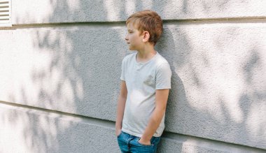 7 yaşındaki çocuğun açık hava portresi. beyaz t-shirt ve kot pantolon çocuk. gündelik kıyafetler giyen çocuk. gri arka planda kafkas çocuk. ciddi çocuk