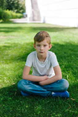 7 yaşındaki çocuk parkta rahatlatıcı. rahat kıyafetler çim üzerinde oturan çocuk