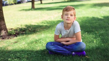 7 yaşındaki çocuk parkta rahatlatıcı. rahat kıyafetler çim üzerinde oturan çocuk