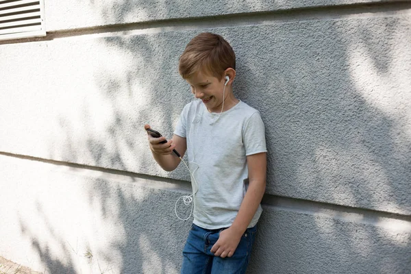 Young boy wearing headphones, looking away. 7 years old boy with smartphone. Portrait of Child blond young boy outdoors. listening music  with headphones