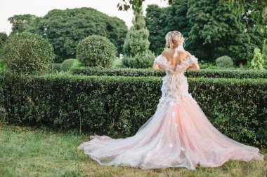 Gelin parkta güzel uzun gelinlik geri döndü var. Parkta yürüyüş vintage beyaz elbiseli güzel şık sarışın gelin. tüyleriyle elbise