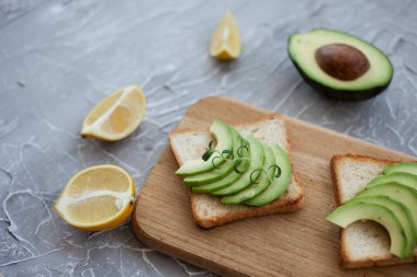 ahşap masada avokado dilimleri ile tost. gri dokulu arka plan üzerinde vintage bıçak ve kaşık. sağlıklı kahvaltı konsepti. limon ve avokado 