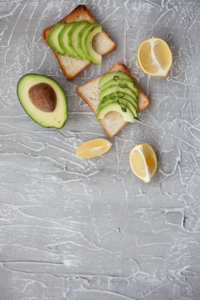 Delicious toast with avocado slices. healthy breakfast concept. lemon and avokado on textured gray background. making sandwiches with avocado healthy organic food top view. flat lay