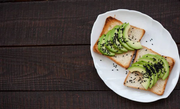 Delicious toast with avocado slices and black sesame. healthy breakfast concept. toast on white plate. making sandwiches with avocado on dark wooden background. healthy organic food top view.
