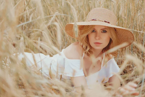 Beauty Girl Outdoors enjoying nature. Beautiful blonde Model girl in white dress on the Summer wheat Field, Sun Light. Girl Outdoors enjoying nature. Happy stylish woman. straw hat