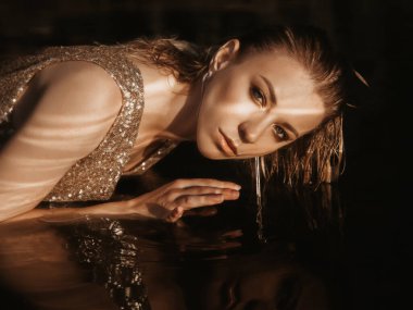 Relaxation and spa concept. Portrait of a fashionable lady in a golden sequin dress. Woman with wet hair and makeup poses in water in natural sunlight. young beautiful european woman clipart