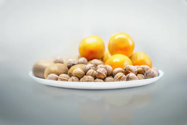 Nozes, kiwi e laranjas em um prato branco — Fotografia de Stock