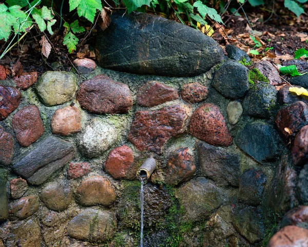 Agua de manantial fresca que corre desde una tubería de metal en un bosque pedregoso s — Foto de Stock