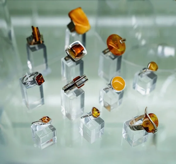 Various silver rings with amber on a glass shelf — Stock Photo, Image