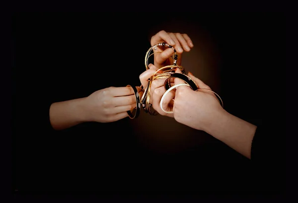 As mãos de duas mulheres com pulseiras douradas em um fundo preto — Fotografia de Stock