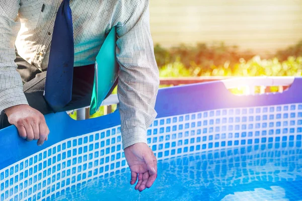 hand of the person in business clothes with the folder touches water in the pool