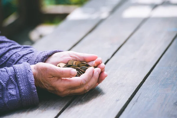 Money, coins, the grandmother on pension and the concept of life, minimum - hands of the old woman to hold a handful of coins on a wooden table