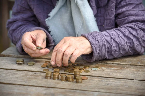 Money, coins, the grandmother on pension and the concept of life, minimum - wrinkled hands of the old woman touch coins on a wooden table