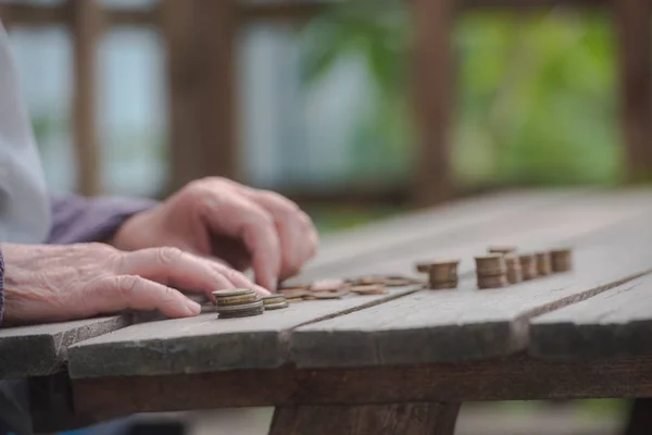 Money, coins, the grandmother on pension and the concept of life, minimum - wrinkled hands of the old woman touch coins on a wooden table