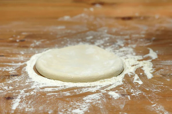 Pizza dough. Basis for baking pizza on a wooden table, close-up