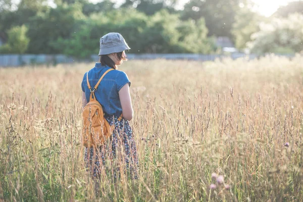 A girl in a dress and hat is walking in the field at sunset. The concept of outdoor recreation.