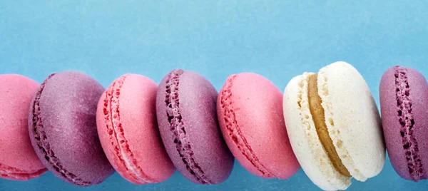 Row of colorful french macarons on blue background. Top view.