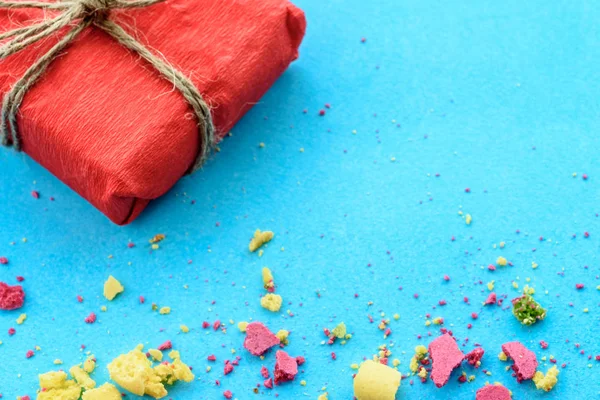 Blue background with gifts and crumbs of a multi-colored cake, top view