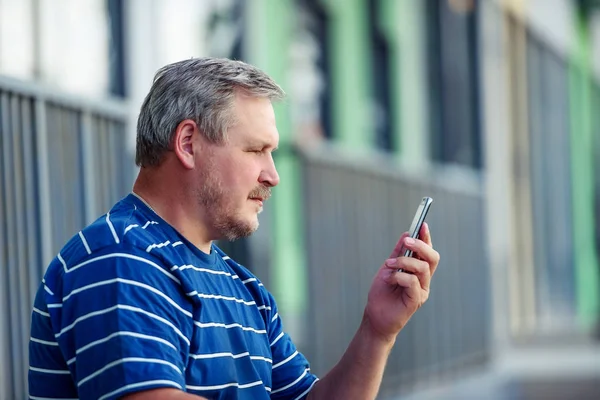 A handsome man reads a message on a smartphone in the city. Close-up portrait.