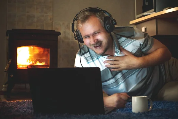Man laughs looking online content on the laptop the night in the living roo