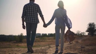 Güneşli bir günde toprak yolda yürürken el ele tutuşan bir çiftin arka görüntüsü. Romantik açık hava yaşam tarzı, HD yatay yavaş çekim videosu. 
