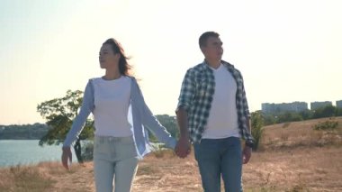 Güneşli bir günde genç bir çift el ele yürür, birbirleriyle konuşur ve gülümserler. Romantik açık hava aşk, bağlantı ve mutluluk anı. 4K yatay video. 