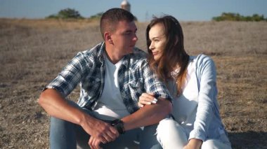 Genç bir çift, romantik bir öpücük vermeden önce doğada oturup birbirlerine sevgiyle bakarlar. Şefkatli bir aşk anı, samimiyet ve bağlantı.. 