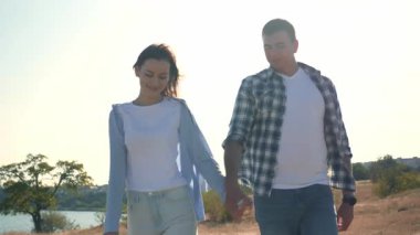 Güneşli bir günde genç bir çift el ele yürür, birbirleriyle konuşur ve gülümserler. Romantik açık hava aşk, bağlantı ve mutluluk anı. 4K yatay video. 