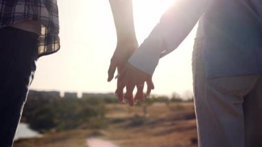 Sıcak güneş ışığında el ele tutuşan genç çiftin yakın çekimi. Romantik ve duygusal an aşkı, samimiyeti, güveni ve birlikteliği simgeler.. 