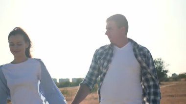 Güneşli bir günde genç bir çift el ele yürür, birbirleriyle konuşur ve gülümserler. Romantik açık hava aşk, bağlantı ve mutluluk anı. 4K yatay video. 