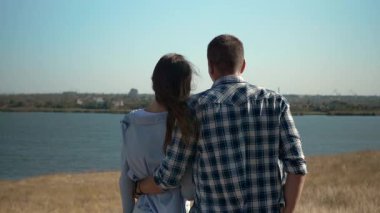 Genç bir çift nehrin kenarında dikiz aynasından kadına sarılıyor doğada romantik bir an, yatay. Yüksek kalite 4k görüntü