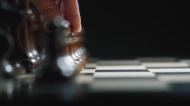 Siyah piyonu satranç tahtasına doğru hareket ettiren bir elin yakın çekimi. Yavaş çekim. 