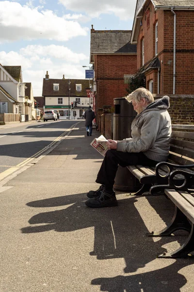 Hombre sentado en el banco leyendo el periódico Sun — Foto de Stock