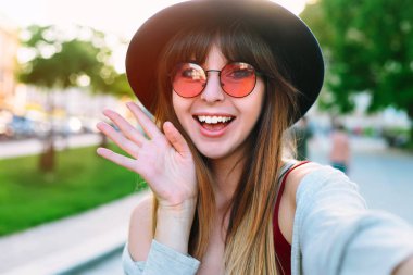 Görüntülü sohbet cep telefonu uygulaması üzerinde konuşmak veya selfie fotoğrafta sosyal medya için sokak gülen kız selfie yapma genç gülümseyen genç mutlu kadın. Kaygısız ve mutlu, güneşli bahar ruh hali. 