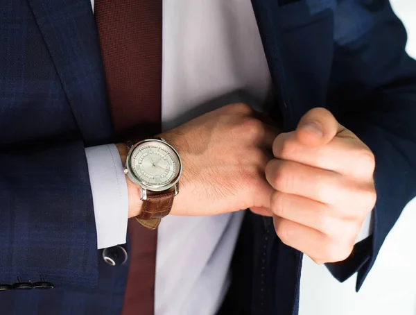 Closeup fashion image of luxury watch on wrist of man.body detail of a business man.Man\'s hand in  pocket closeup at white background.Man wearing blue jacket and white shirt and tie.