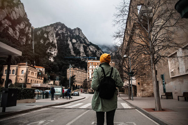 Young female traveler with hat and backpack standing in Monserrat square with tower and basilica Back view.Discovering Europe