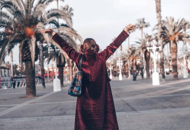 Görünümü hippi kız elle yedeklemek kadar sıkılmış ceket, çanta ve şehir manzarası üzerinde etkilidirler alay kadar giymiş. Gezgin kentsel arka plan üzerinde. El kaldırdı. Turist Barcelona, sakin yaşam tarzı