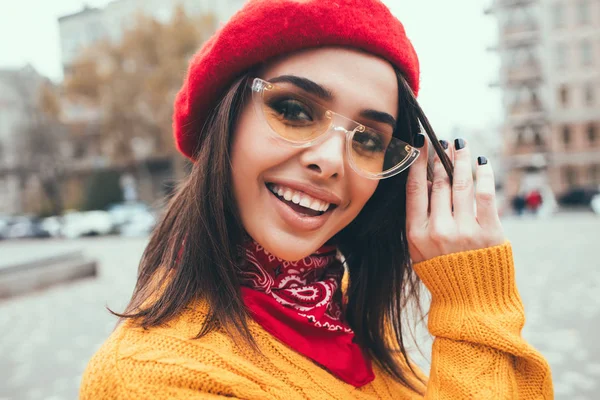赤いベレー帽とトレンディな黄色いセーターを着て街でカメラに笑顔でかわいい女の子の Europe Portrait で良い一日でポジティブなエネルギーを表現する明るいメイクと素晴らしい白い女性モデルのポートレート — ストック写真