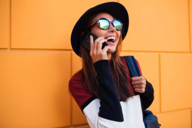 Açık havada akıllı telefon kullanan sürpriz genç kadın. Cep telefonu üzerinde konuşurken ışınlama gülümseme ile güzel bir kadın. Oturma ve telefonu konuşurken neşeli kadın. Açık havada çekim yatay