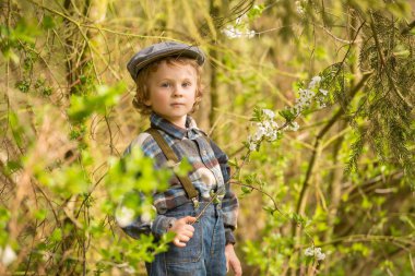 Baharda çiçek açan bahçede poz veren genç sarışın çocuk..