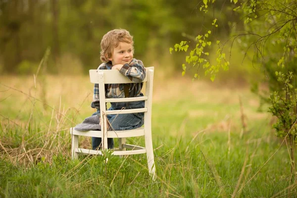 年轻的金发碧眼的男孩在户外的白杨树下 坐在白色的旧椅子上休息 — 图库照片