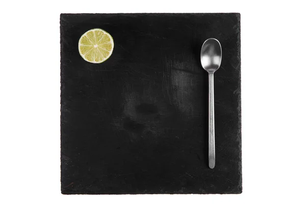 Silver spoon lie on the black stone tile of the plate — Stock Photo, Image