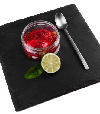 Beyaz bir arka plan üzerinde siyah bir taş plaka üzerinde bir kavanozda Ahududu cheesecake tatlı