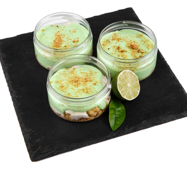 Lime cheesecake dessert in a jar on a black stone plate on a white background