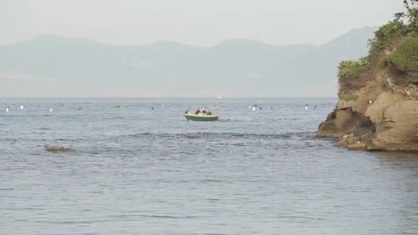 Un petit bateau naviguant le long de la mer, sur le fond d'une île aux montagnes — Video