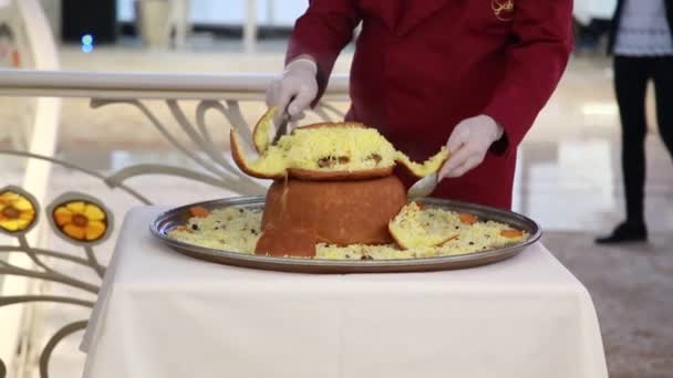 Close-up van een chef-kok die een stevige schotel snijdt - pilaf gebakken in brood — Stockvideo